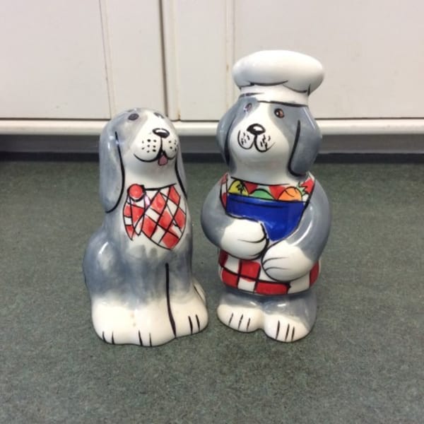 Two ceramic dog-shaped salt and pepper shakers, one wearing a chef's hat and holding a bowl.