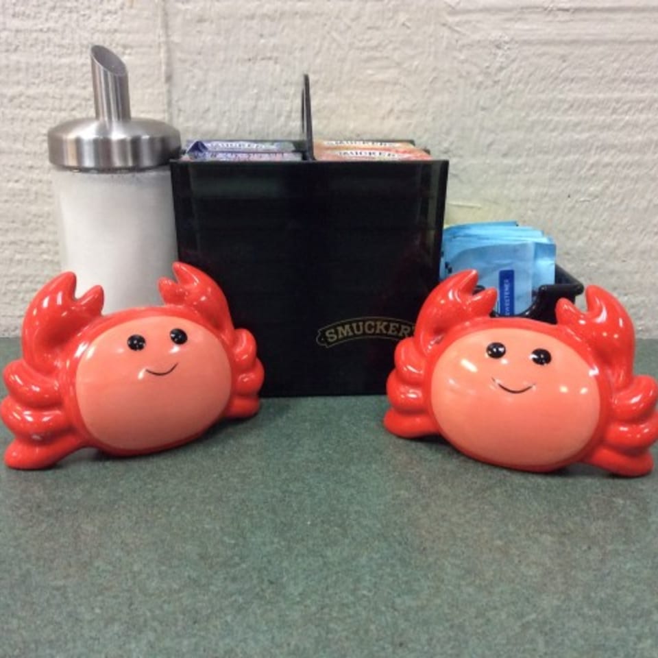 Two smiling red crab figurines flank a sugar dispenser and a Smucker's caddy on a green table.