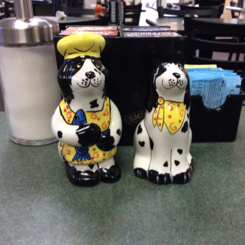 Two dog-shaped ceramic figurines, one wearing a chef's hat, on a cafe table.