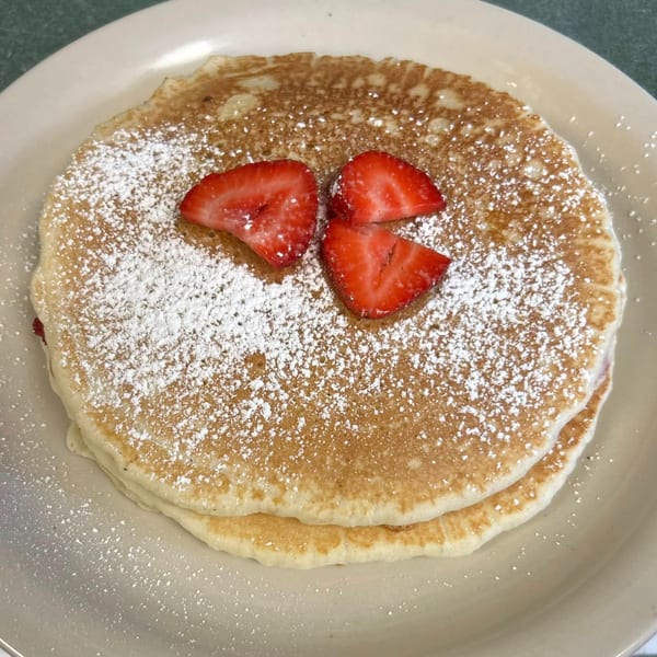 Fluffy pancakes from Shakers American Café, dusted with powdered sugar and topped with fresh strawberries.