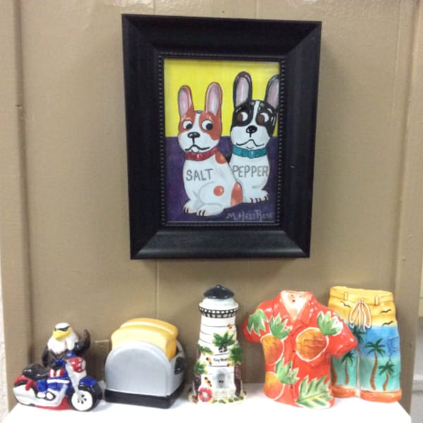 A framed painting of two dogs labeled "Salt" and "Pepper" hangs above various decorative figurines.