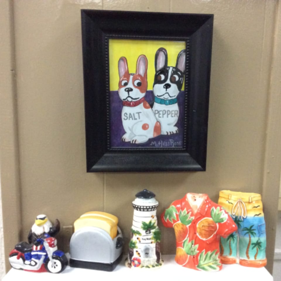 A framed painting of two dogs labeled "Salt" and "Pepper" hangs above various decorative figurines.