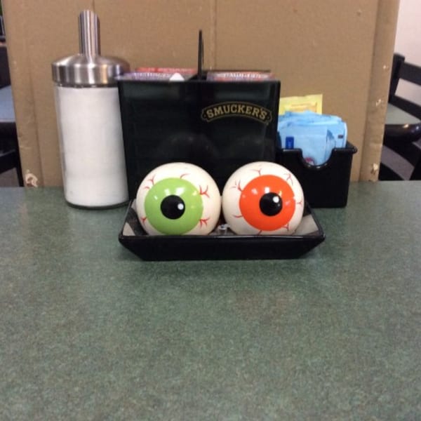 Two eyeball-shaped salt and pepper shakers, one green and one orange, on a cafe table.