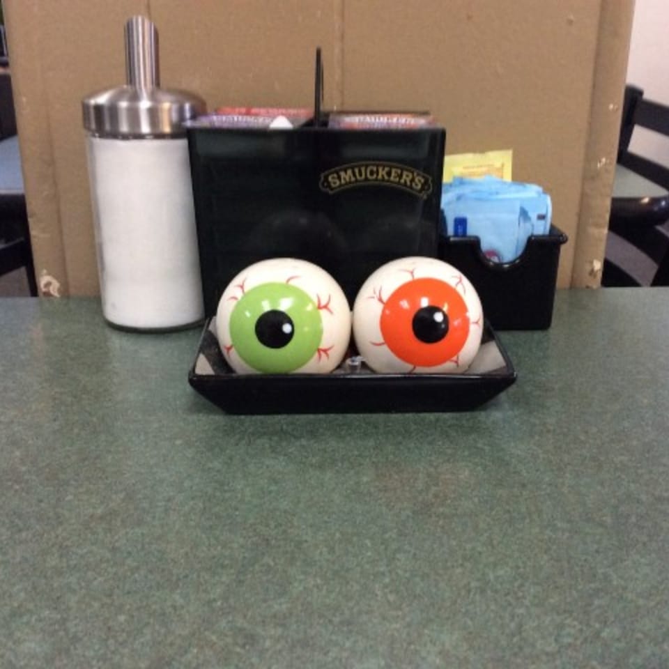 Two eyeball-shaped salt and pepper shakers, one green and one orange, on a cafe table.