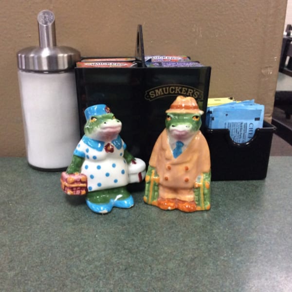 Frog salt and pepper shakers, sugar dispenser, and condiment caddy on a cafe table.