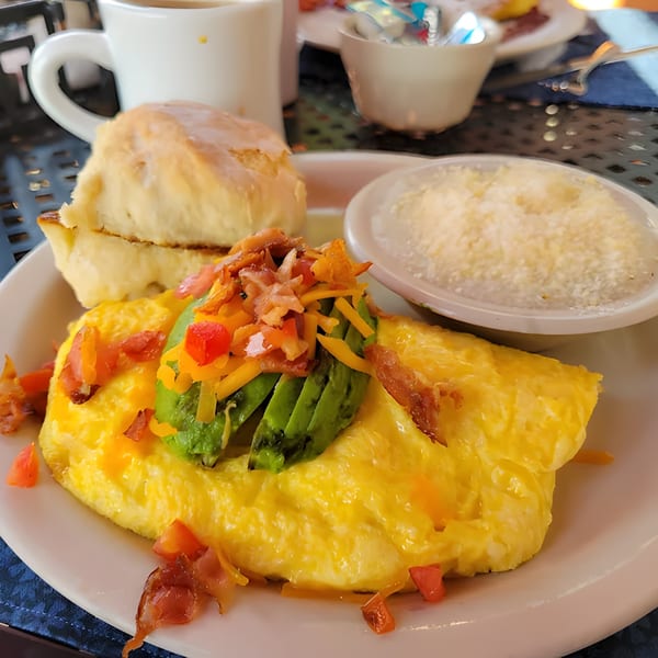 A Shakers American Café breakfast with an omelet, biscuit, and grits on a white plate.