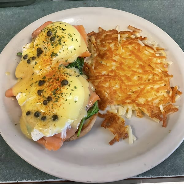 Eggs Benedict with smoked salmon, capers, and hash browns on a white plate at Shakers American Café.