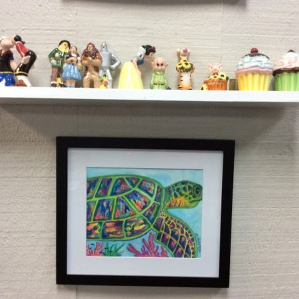 A shelf with various cartoon figurines and cupcake decorations above a framed colorful sea turtle painting.