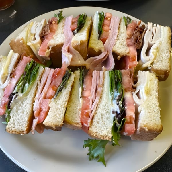 A large club sandwich, cut into triangles, with various meats, lettuce, and tomatoes on a white plate.